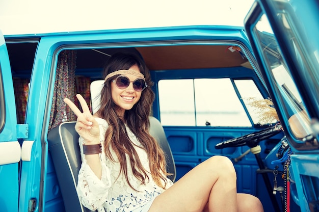 summer holidays, road trip, vacation, travel and people concept - smiling young hippie woman showing peace gesture in minivan car