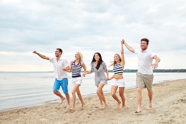 лето, праздники, море, туризм и концепция людей - группа улыбающихся друзей в солнцезащитных очках, бегущих по пляжу