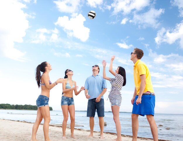Photo summer holidays, sport, leisure and people concept - group of happy friends playing beach ball