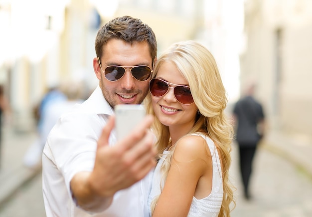 summer holidays, technology, love, relationship and dating concept - smiling couple taking picture with smartphone in the city