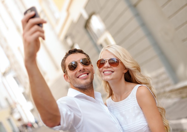 summer holidays, technology, love, relationship and dating concept - smiling couple taking picture with smartphone in the city