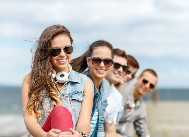 summer holidays and teenage concept - smiling teenage girl in sunglasses hanging out with friends outdoors