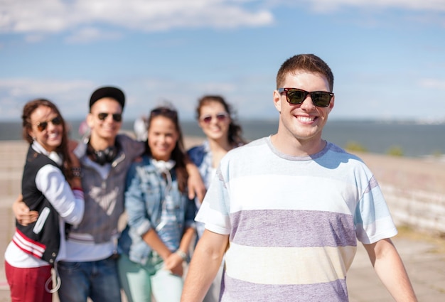 летние каникулы и подростковая концепция - мальчик-подросток в солнечных очках тусуется с друзьями на улице