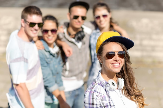 summer holidays and teenage concept - teenage girl in sunglasses, cap and headphones hanging out with friends outside