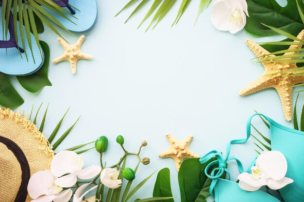 Summer holidays and travel concept palm leaves hat flip flop and shells on blue background flat lay with copy space