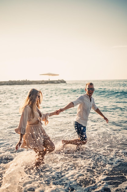 Летние каникулы и путешествия Сексуальная женщина и мужчина в морской воде на закате Влюбленная пара отдыхает на пляже восхода солнца Любовные отношения пары, наслаждающейся летним днем вместе