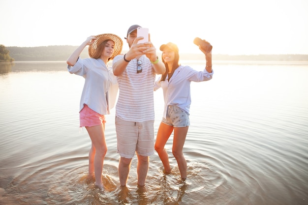 夏、休日、休暇、幸福の概念-スマートフォンで自分撮りをしている友人のグループ。