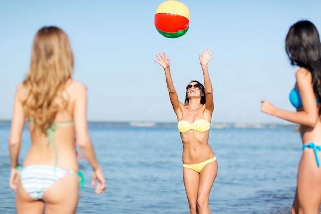 summer holidays, vacation and beach activities concept - girls in bikinies playing ball on the beach