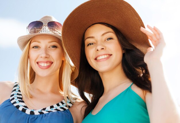 Vacanze estive e concetto di vacanza - ragazze con i cappelli sulla spiaggia