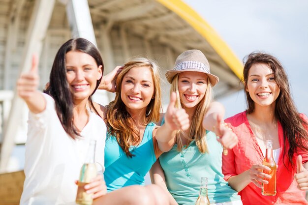 summer holidays and vacation - girls with drinks showing thumbs up on the beach