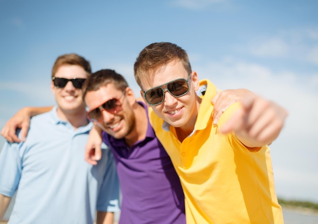 Photo summer, holidays, vacation and happiness concept - group of friends having fun on the beach and pointing at you