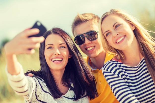 лето, праздники, каникулы, концепция счастливых людей - группа друзей, фотографирующих со смартфоном
