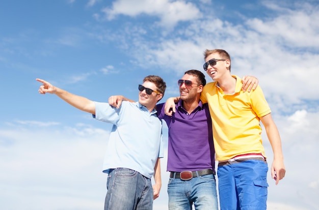 summer, holidays, vacation, happy people concept - group of male friends walking on the beach pointing finger somewhere