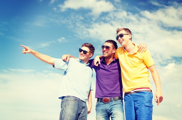 summer, holidays, vacation, happy people concept - group of male friends walking on the beach pointing finger somewhere