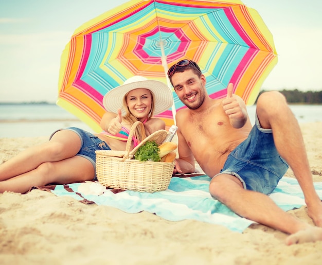 여름, 휴일, 휴가, 행복한 사람들 개념 - 화려한 우산 아래 해변에 누워 엄지손가락을 치켜드는 웃고 있는 커플