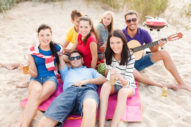 Foto estate, vacanze, vacanze, musica, concetto di persone felici - gruppo di amici con la chitarra che si divertono sulla spiaggia