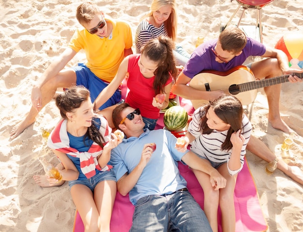 лето, праздники, каникулы, музыка, концепция счастливых людей - группа друзей с гитарой, веселящихся на пляже