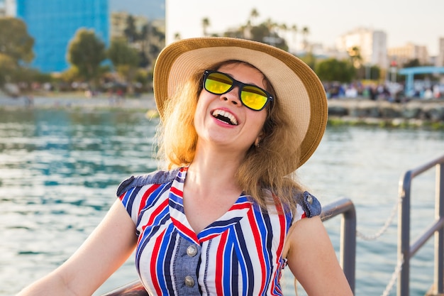 Summer holidays, vacation, travel and people concept - smiling laughing young woman wearing sunglasses and hat on beach over sea.