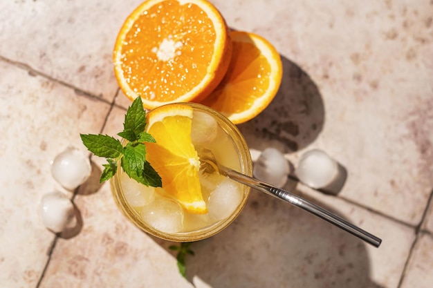 Summer iced cocktail with orange and mint with metal straw on beige tile background Top view