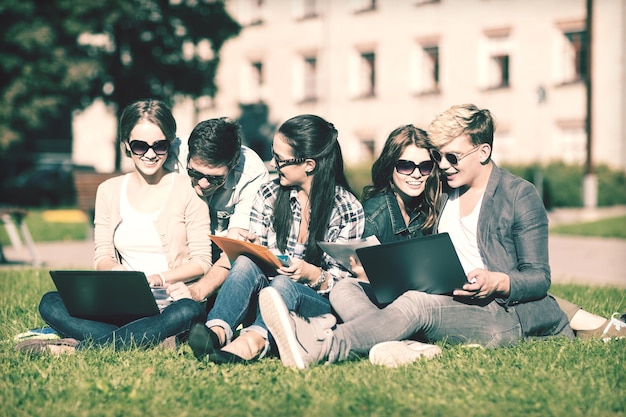 Photo summer, internet, education, campus and teenage concept - group of students or teenagers with laptop, notebooks, files and folders