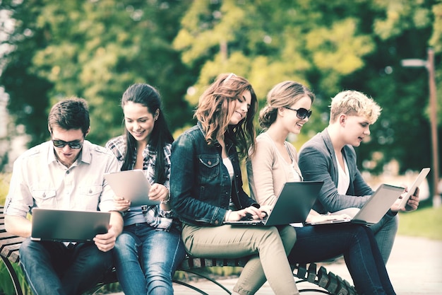 summer, internet, education, campus and teenage concept - group of students or teenagers with laptop and tablet computers hanging out