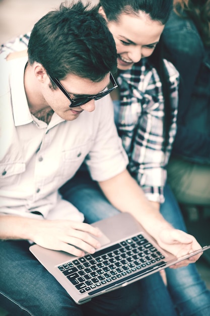 summer, internet, education, campus and teenage concept - students or teenagers with laptop computer hanging out