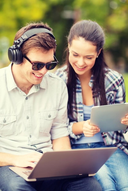 summer, internet, education, campus and teenage concept - students or teenagers with laptop and tablet computers hanging out