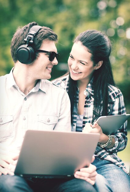 summer, internet, education, campus and teenage concept - students or teenagers with laptop and tablet computers hanging out