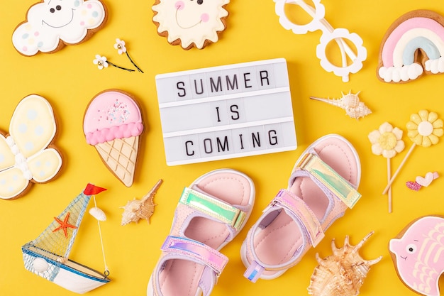 Summer is coming Motivational quote on lightbox and cute summer symbols on yellow background Top view Flat lay Creative inspirational summer concept