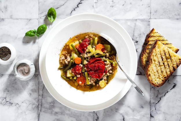 Summer italian minestrone soup with tomatoes and homemade bread on a marble table