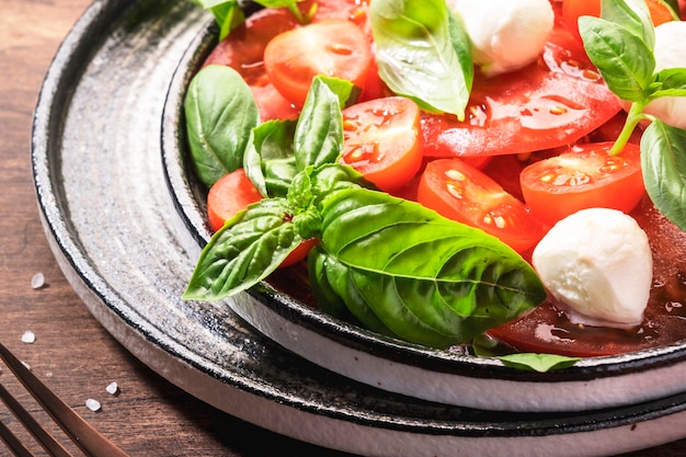 Summer italian salad Caprese with red tomatoes and mozzarella cheese with green basil leaves and olive oil dressing Top view wooden table