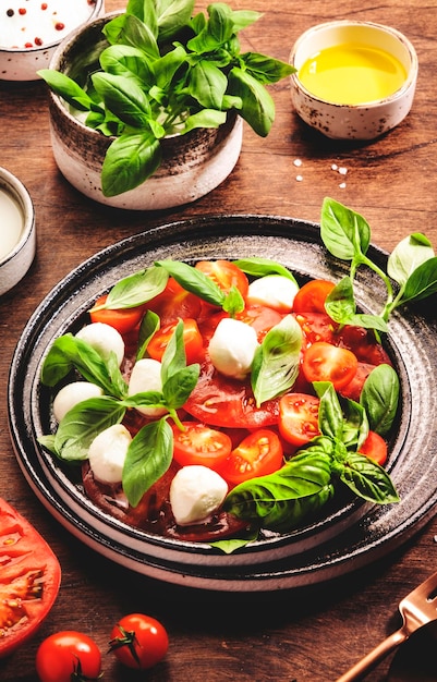 Summer italian salad Caprese with red tomatoes and mozzarella cheese with green basil leaves and olive oil dressing Top view wooden table