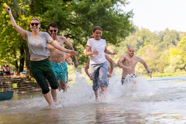 Летняя радость группа счастливых друзей, весело проводящих время, бегая и плескаясь на реке