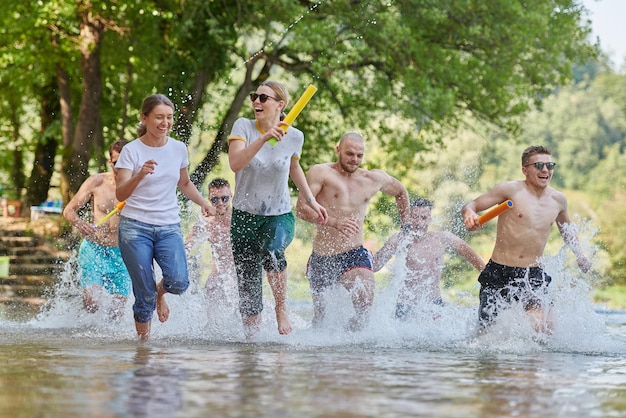 Summer joy group of happy friends having fun while running and splashing on river