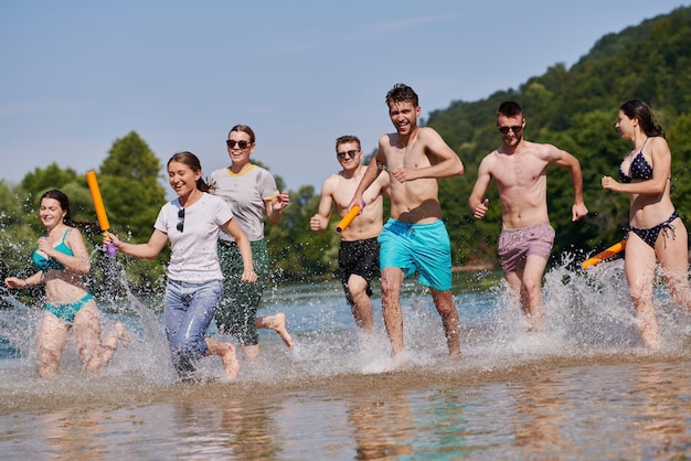 Summer joy group of happy friends having fun while running and splashing on river