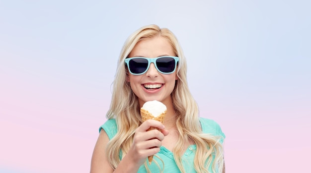 summer, junk food and people concept - young woman or teenage girl in sunglasses eating ice cream over rose quartz and serenity gradient background