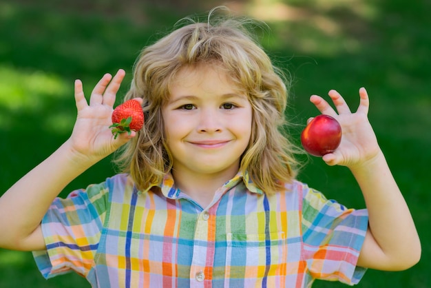 Summer kid face summer berry for kids cute little boy eating strawberry making funny faces and playi