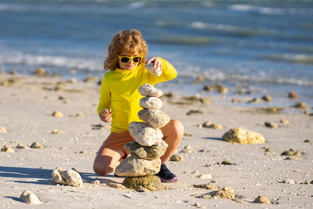 Photo summer kid meditation little child playing with stones on the beach child play with pyramid of stone