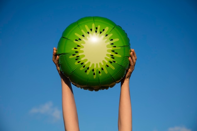 Summer kiwi fruit balloon held in the air against a bright blue summer sky