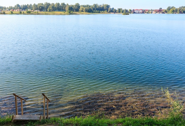 Летний спокойный пляж озера с деревянными обрывами к воде