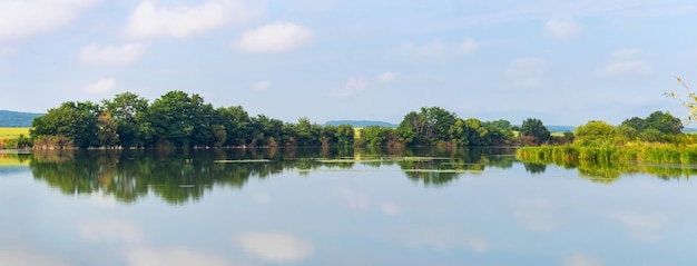 Summer landscape panorama with river and trees reflected in river water