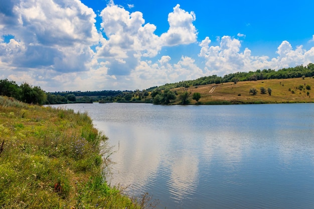 Фото Летний пейзаж с красивым озером, зелеными лугами, холмами, деревьями и голубым небом