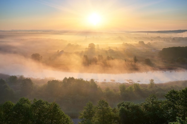 Summer landscape with fog over the river. The first rays of the rising sun paint mist