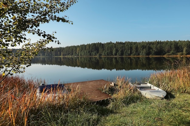 Summer landscape with lake woods on sky horizon wooden jetty and boat