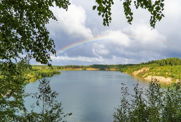 Summer landscape with a rainbow in the distance over the forest and water