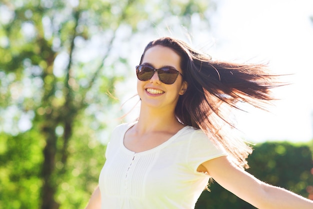 summer, leisure, vacation and people concept - smiling young woman wearing sunglasses standing in park