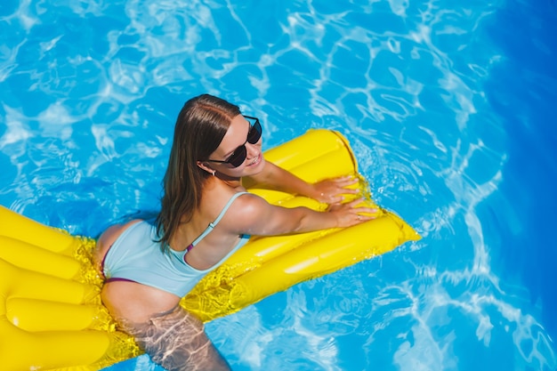 Summer lifestyle portrait of beautiful woman in sunglasses floating on inflatable mattress in outdoor swimming pool Summer vacation on a tropical island