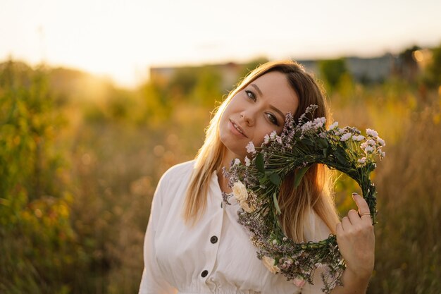 Summer lifestyle portrait of beautiful young woman in a wreath of wild flowers wreath on his head