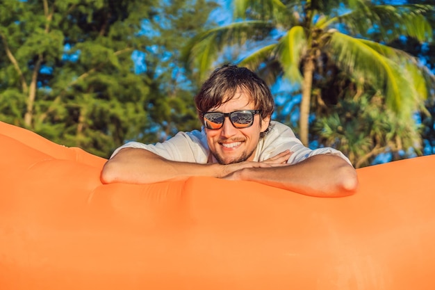 Foto ritratto di stile di vita estivo di un uomo seduto sul divano gonfiabile arancione sulla spiaggia dell'isola tropicale rilassarsi e godersi la vita sul letto ad aria