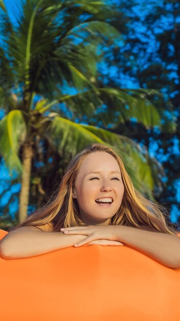 해변에 있는 주황색 소파에 앉아 있는 예쁜 여자의 여름 라이프스타일 초상화